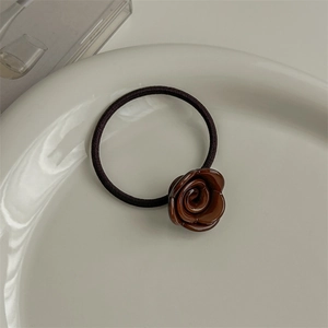 Detail of a glossy brown resin rose flower hair tie placed on a white ceramic plate