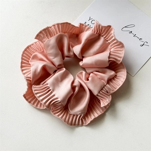 Detail of light pink pleated satin scrunchie with soft ruffled edges on a beige background