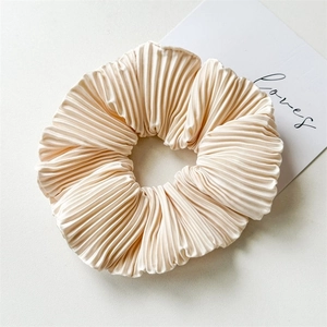 Macro shot of cream-colored pleated satin scrunchie with detailed accordion fold texture