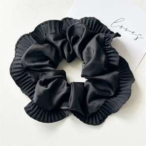 Detailed view of the pleated black satin hair scrunchie with ruffled edges and silky texture