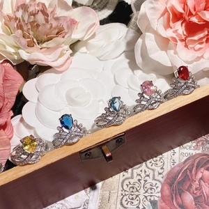 Set of five silver crown rings with colorful pear-shaped gemstones on a wooden box