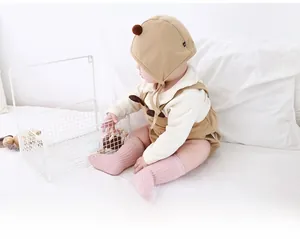 Detail of warm brown corduroy baby overalls with cream white knit sweater and pompom hat