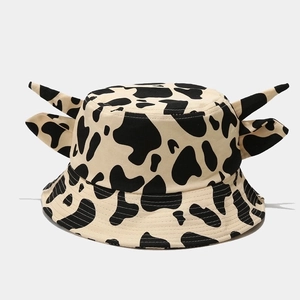 Detail of cartoon cow print bucket hat featuring 3D ears and horns on a grey surface