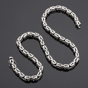 Polished silver stainless steel Byzantine king chain necklace on black reflective surface