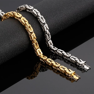 Detail of woven stainless steel chain necklaces in gold and silver on a reflective surface