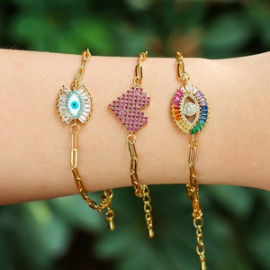 Three gold bracelets featuring evil eye and heart charms worn on a person's wrist