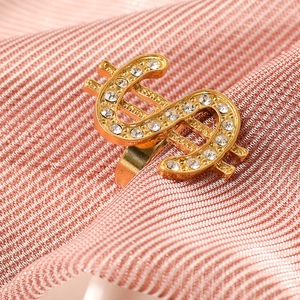 Close-up of golden dollar sign ring encrusted with white rhinestones on striped fabric