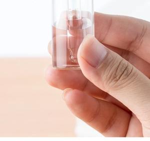 Close-up of hand holding a glass dropper bottle with wood grain cap for essential oils