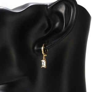 Detailed view of a gold hoop earring featuring a rectangular zircon pendant on a model