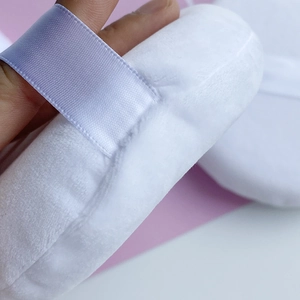 Close-up of white velvet body powder puff with light blue ribbon strap for makeup