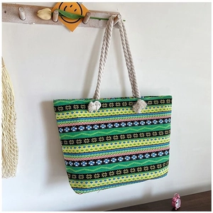 Detailed view of leaf pattern canvas beach bag with beige cotton rope handles hanging on hook
