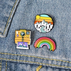 Detailed view of colorful enamel pins with landscape, camera, and rainbow designs on denim