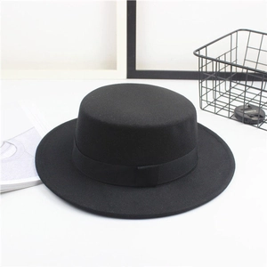 Detail shot of a black wool felt flat top hat with ribbon on a decorative white desk