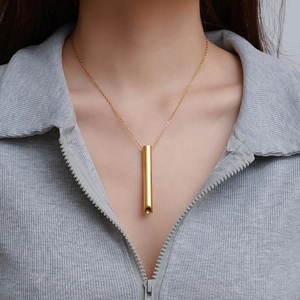 Polished 18K gold-plated cylindrical whistle necklace worn over a grey zip-up hoodie