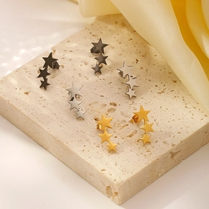 Three-star stainless steel stud earrings in black, silver, and gold on marble background