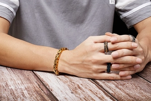 Gros plan d'un bracelet byzantin doré pour homme et de bagues sur une table en bois