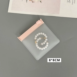 Detailed close-up of pink translucent 8x8cm jewelry storage bag with pearl earrings