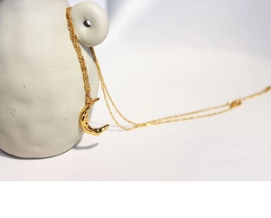 Detailed view of gold moon necklace with hammer textured surface on ceramic stand