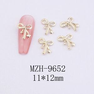 Detail view of 11x12mm golden bow nail charms and demonstration on pink manicure