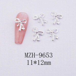 Macro shot of silver bow nail charms with inlaid stones on pink mannequin nails
