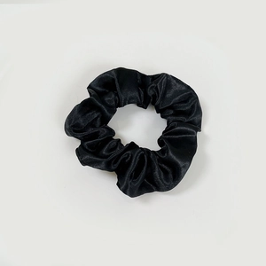 Macro shot of black satin scrunchie showing smooth texture and elastic pleats detail