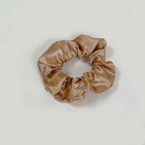 Detailed close-up of champagne gold satin scrunchie showing glossy pleated silk texture