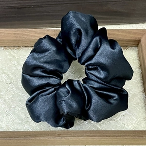 Close-up of black satin scrunchie with smooth silk texture and elegant vintage folds