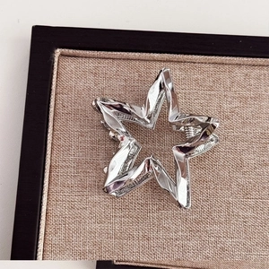 Detailed view of silver liquid metal star hair claw clip on beige fabric display