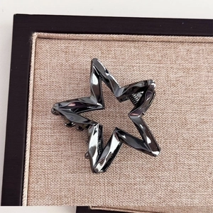 Macro shot of gun-black star-shaped metal hair claw clip on beige textured board