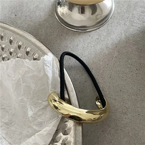 Macro detail of glossy golden minimalist metal ponytail cuff with black elastic band