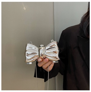 Silver bow evening clutch bag with metallic finish and thin chain strap held by model