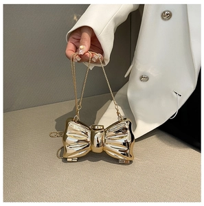Detail of a golden bow-shaped metal clutch bag with a sleek chain strap on a white suit
