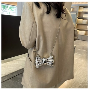 Modern silver metallic bow evening bag with elegant chain strap shown on beige blazer