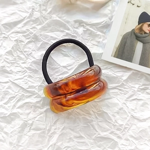 Detail of amber tortoiseshell patterned acrylic wavy hair tie on a white background