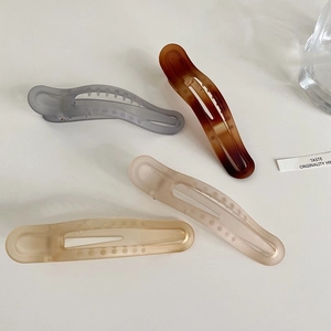 Close-up of four matte duckbill hair clips in amber, blue, cream, and champagne colors
