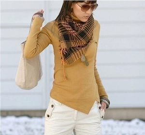 Detail of a mustard knit sweater with asymmetric hem and houndstooth scarf on model outdoors
