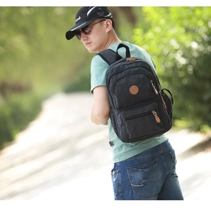 Detail of multi-compartment canvas backpack with leather zipper pulls and logo patch