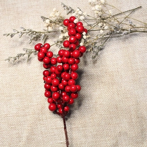 Close-up of artificial red berry stem on rustic burlap background with dried flowers