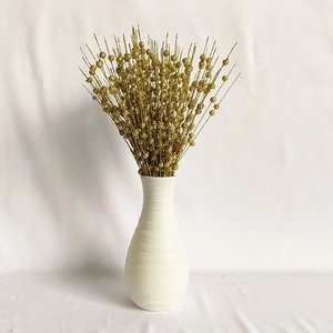 Close-up of golden glitter berry stems with decorative beads in a white ceramic vase