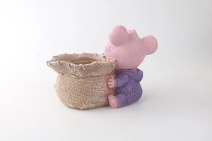 Dettaglio di orsetto in resina rosa con maglione viola che tiene un vaso a forma di sacco