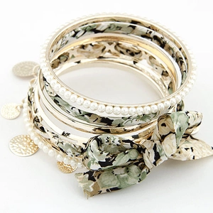 Detail von geschichteten Armbändern mit Blumenband, Goldringen und weißen Perlen