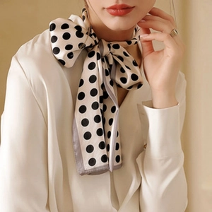 Dettaglio di un elegante foulard di seta a pois neri annodato sul collo della modella