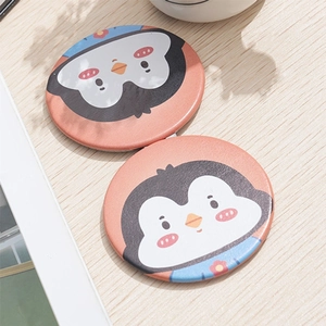 Close-up of portable folding mini makeup mirror with cute cartoon penguin on pink background