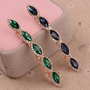 Close-up of leaf-shaped metal hair claws with green and blue crystals on pink velvet box