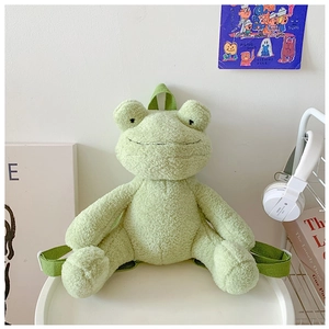 Detailed close-up of a plush green frog backpack on a white table with minimalist decor