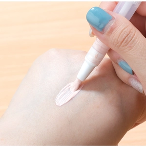 Detail showing hand applying liquid concealer from a white twist pen with brush tip