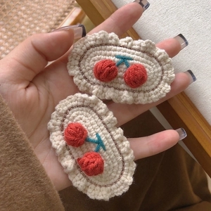 Detail of beige woven hair clips with red cherry knit patterns and gold thread edging
