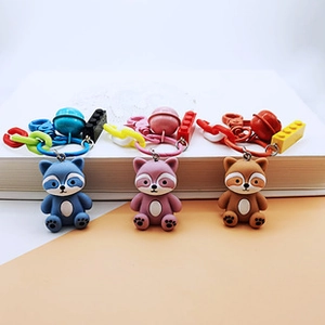 Three cute raccoon silicone keychains in blue, pink, and brown with bells and charms