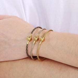 Detailed view of twisted steel cable bracelets with gold metal beads worn on a model wrist