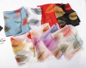 Flat lay of multiple colorful 100% silk leaf pattern scarves on white background